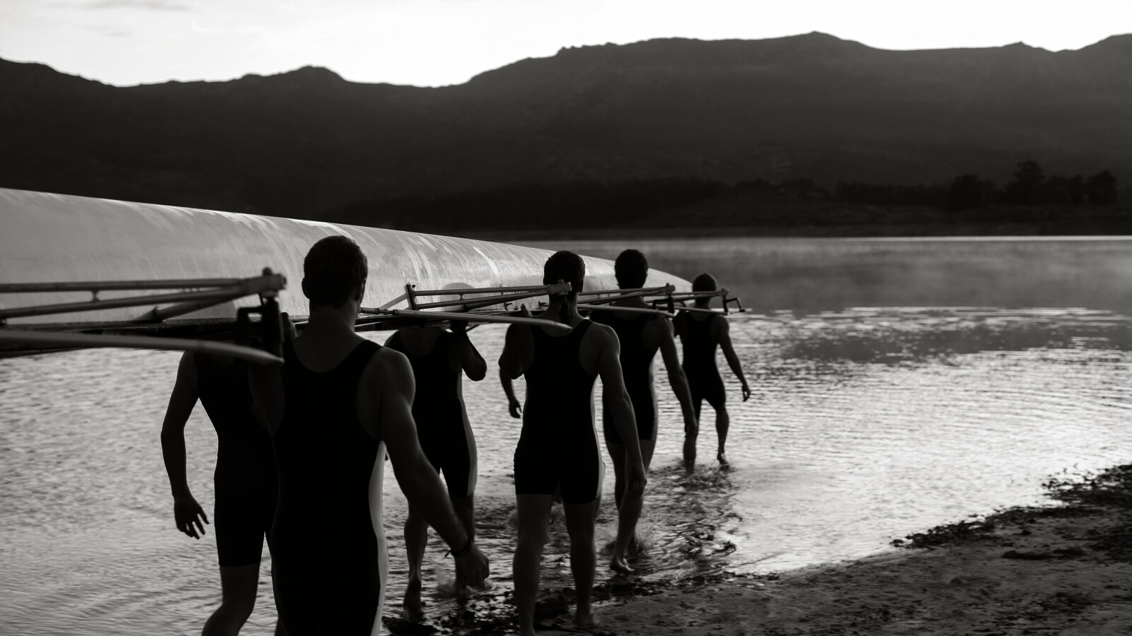 A rowing crew carrying their shell into the water together at dawn